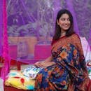 Home Young woman wearing a colorful floral saree, sitting outdoors with a joyful smile.